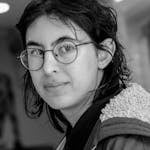 Black and white close-up portrait of an adult wearing glasses and a coat indoors.