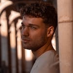 Portrait of a contemplative man leaning against a pillar, bathed in sunset light.